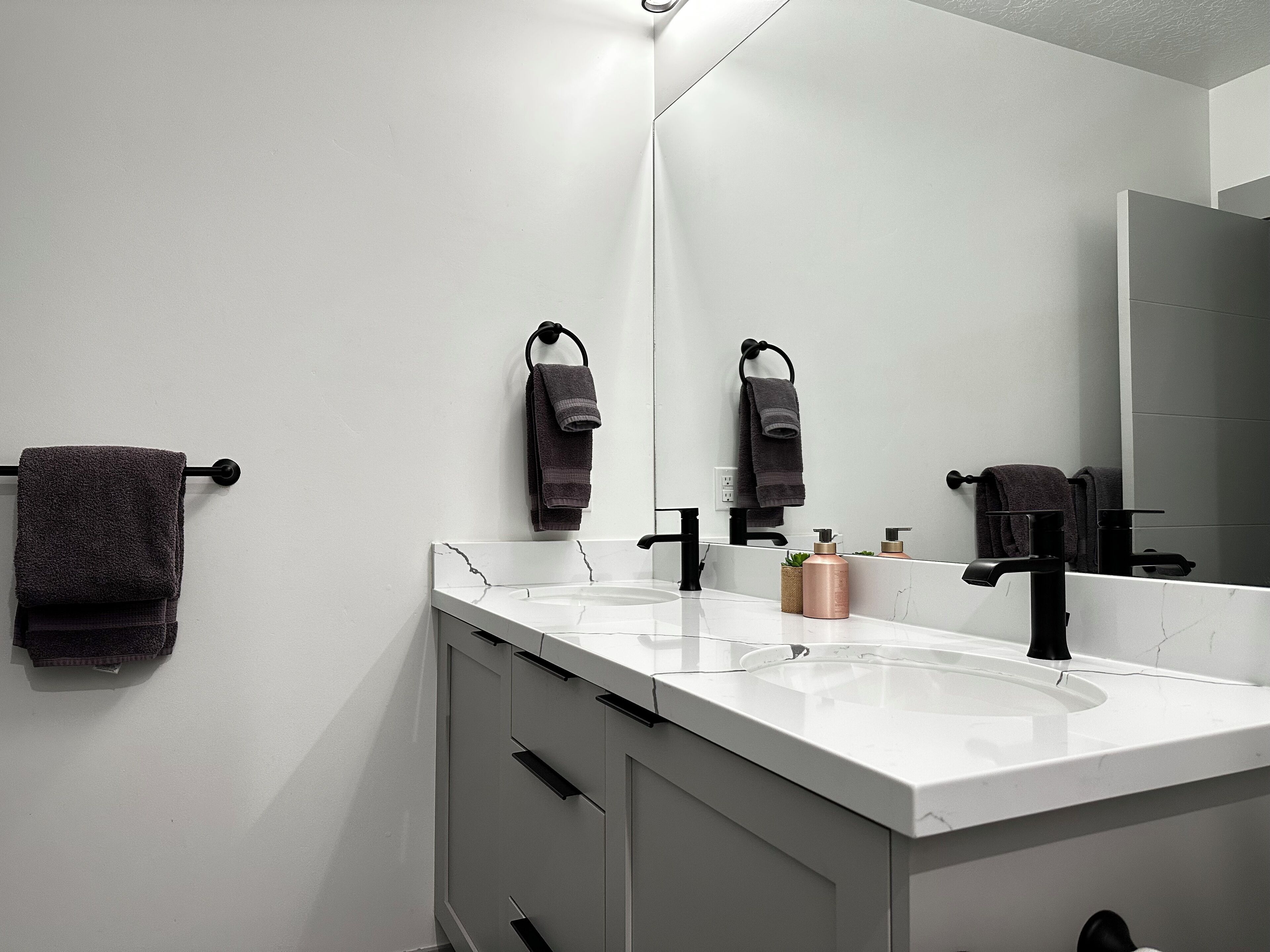 A modern bathroom with two sinks, black faucets, and a large mirror.