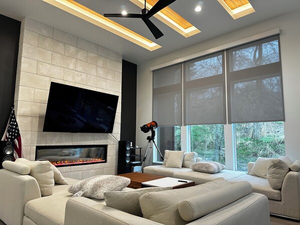 Un salón moderno con chimenea, ventanas amplias y un televisor de pantalla plana.