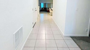 A hallway with white walls and tiled flooring leading to a room with a bed and a window. - Den Haven 15 Min From DIA 3 En Suite Bedrooms (Denver)