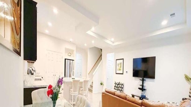 A modern living room with a glass dining table, white sofas, and a TV mounted on the wall. - Den Haven 15 Min From DIA 3 En Suite Bedrooms (Denver)