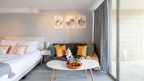 Moderni hotellihuone, jossa on sänky, sohva, sohvapöytä ja taideteoksia seinällä.
