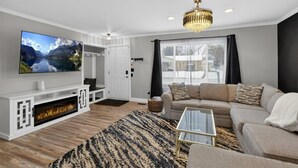 A modern living room with a flat-screen TV, a fireplace, a sofa, and a chandelier. - Charming 3-bedroom house in excellent Troy with AC (Troy)