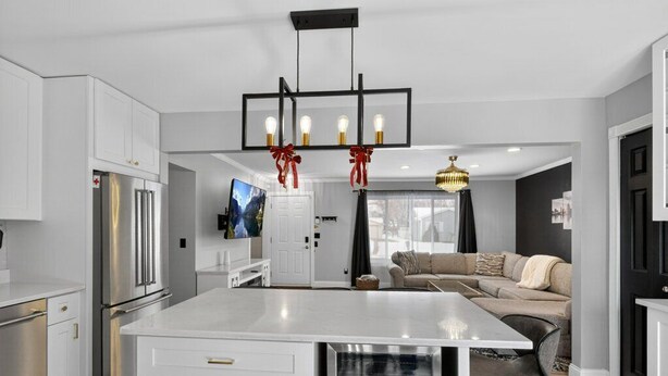 A modern kitchen with white cabinetry, a central island, stainless steel appliances, and a pendant light with red ribbons. - Charming 3-bedroom house in excellent Troy with AC (Troy)