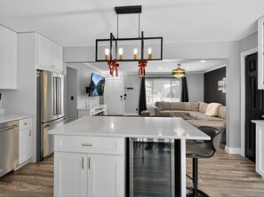 Een moderne keuken met witte kasten, een centraal eiland, roestvrijstalen apparatuur en een hanglamp versierd met rode linten.