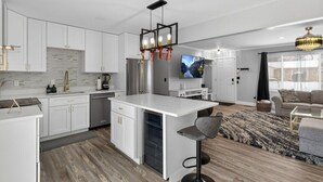 A modern kitchen with white cabinets, a central island, and a dining area with a TV. - Charming 3-bedroom house in excellent Troy with AC (Troy)