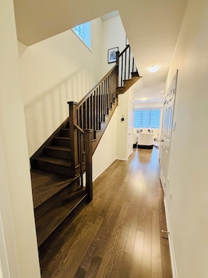 Un escalier avec des marches en bois et des rampes noires menant à une pièce dotée d’une porte blanche et d’une fenêtre avec des stores.