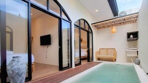 Een modern buitengebied met een jacuzzi, een houten terras en glazen deuren die leiden naar een woongedeelte.