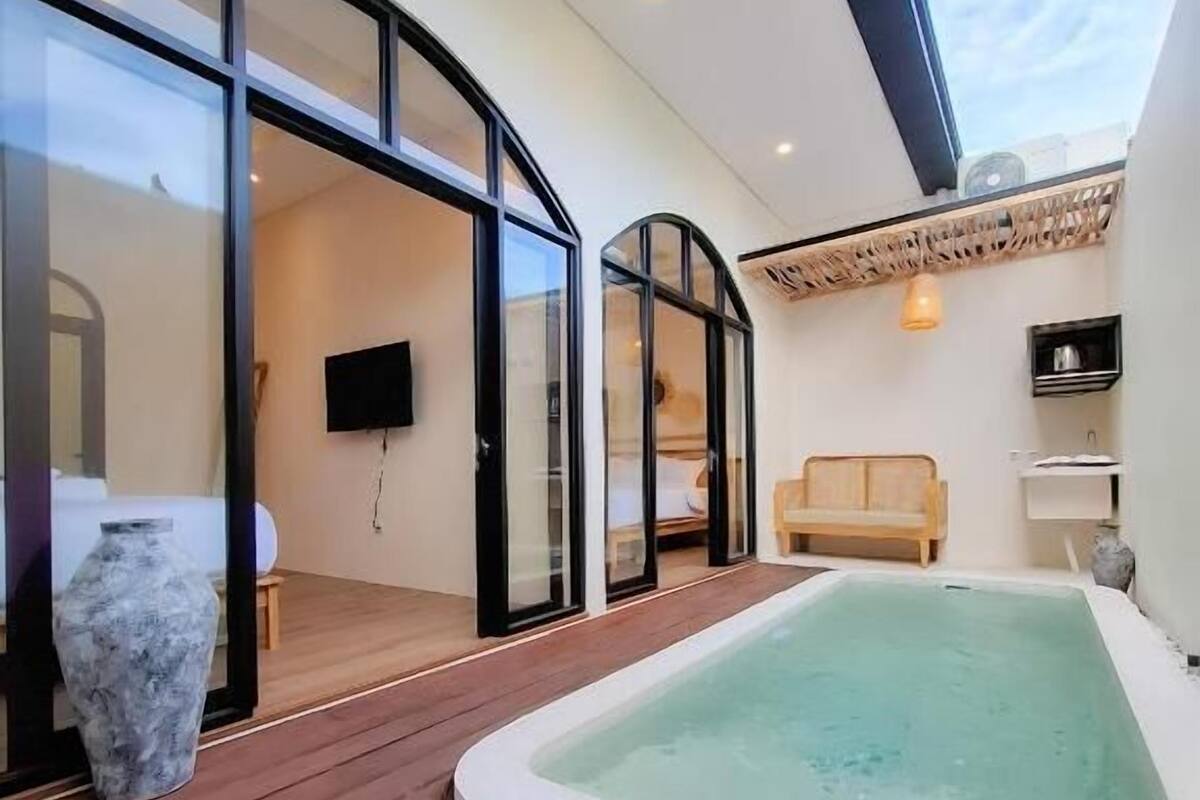 Un espacio exterior moderno con un jacuzzi, terraza de madera y puertas de cristal que dan a un salón.