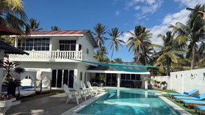 Uma casa de dois andares com piscina, fachada branca e varanda.