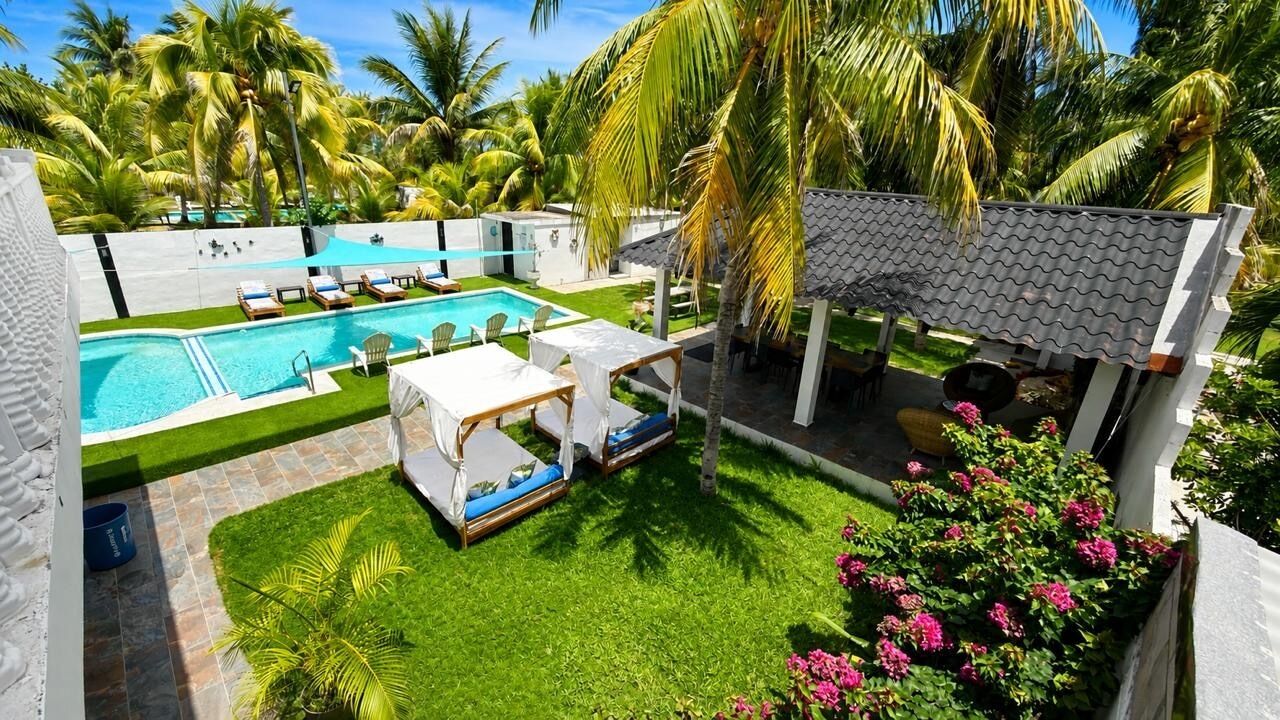 Une piscine avec des chaises longues, un espace de repos couvert et une végétation luxuriante.