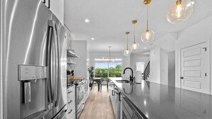 Cozinha moderna com eletrodomésticos de aço inoxidável, uma ilha central, iluminação pendente e vista para o exterior.