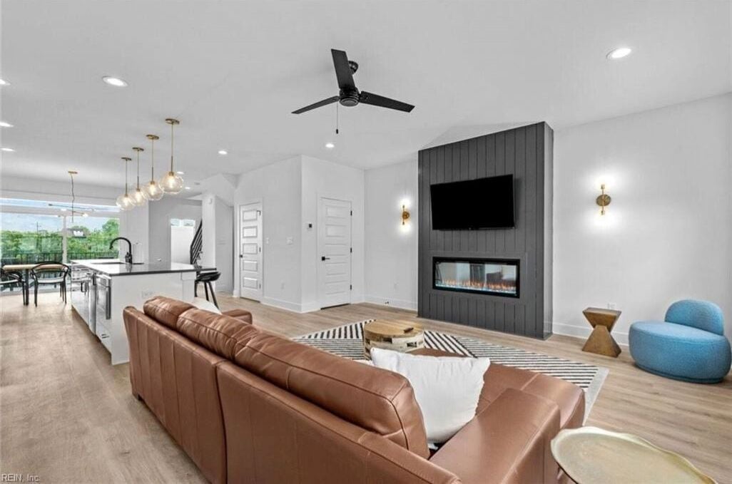 Ein modernes Wohnzimmer mit einer braunen Ledersofa, einem flachbildfernseher an der Wand und einem Deckenventilator.