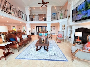 A spacious living room with a high ceiling, a central coffee table, and a television mounted above a fireplace. - Ultimate Lake Hamilton Estate 15 Bedrooms Private Resort on 8 Acres SLEEPS 53 (Hot Springs)
