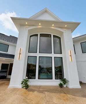 A modern house with a large central bay window, a flat roof, and a small porch with potted plants. - Ultimate Lake Hamilton Estate 15 Bedrooms Private Resort on 8 Acres SLEEPS 53 (Hot Springs)