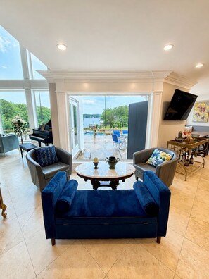A spacious living room with a view of a pool and lake, a piano, and a dining area with a TV. - Ultimate Lake Hamilton Estate 15 Bedrooms Private Resort on 8 Acres SLEEPS 53 (Hot Springs)