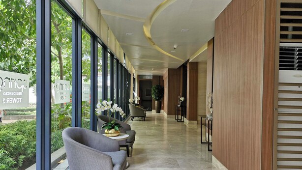 Un hall d’hôtel au design moderne, comprenant un comptoir d’accueil, un espace salon avec des fauteuils et de grandes fenêtres offrant une vue sur la verdure.