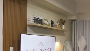 Un salon moderne avec un téléviseur à écran plat fixé au mur, un bureau en bois, une chaise noire et une étagère décorative au-dessus du bureau.