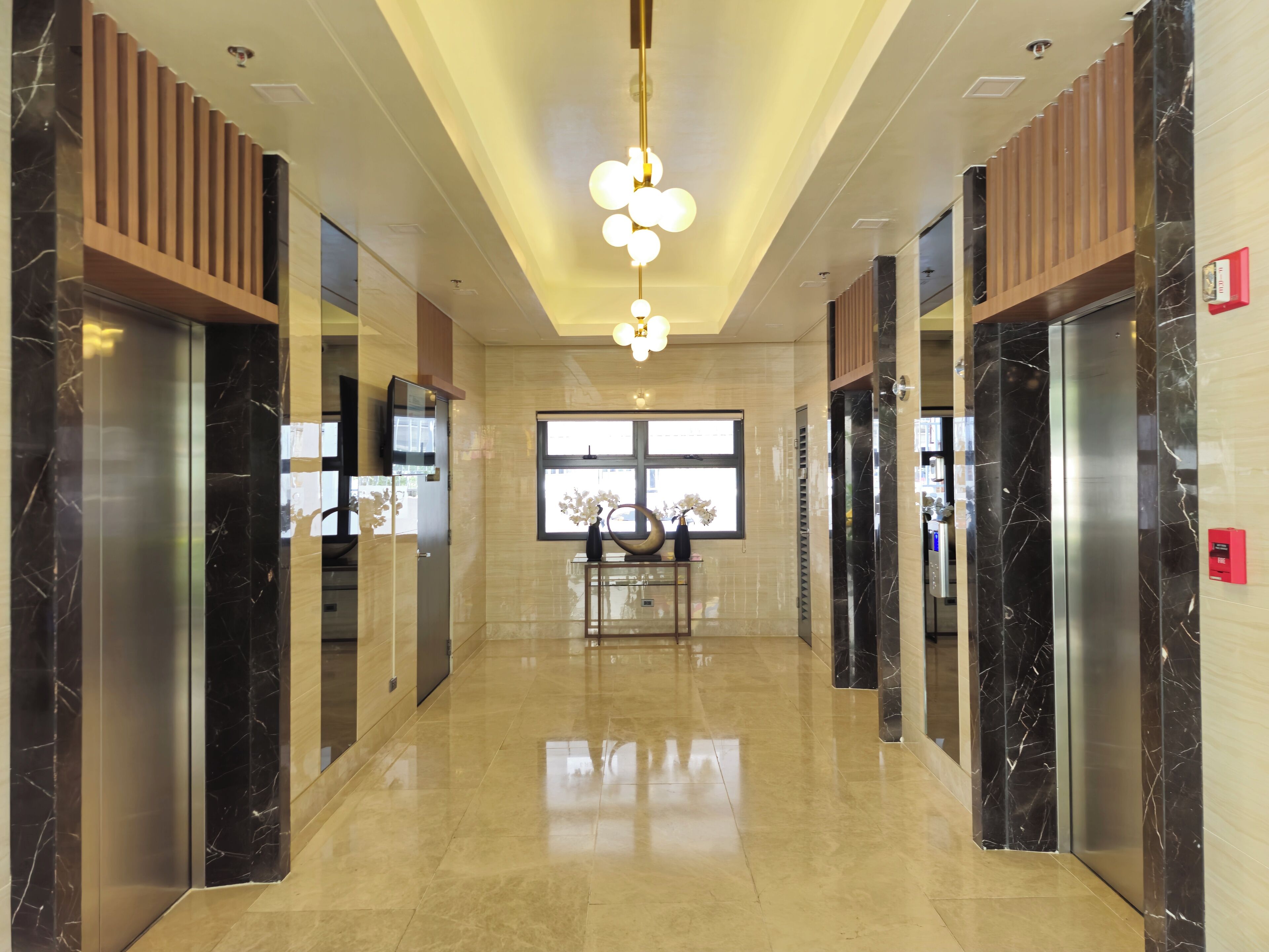 A modern hallway with elevators, marble flooring, and a central decorative light fixture.