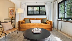 A cozy living room with a sofa, a coffee table, and a window with curtains. - Serene Mill Valley Retreat - King Bed, Walk to Downtown, Deck, Sleeps 4. (Mill Valley)