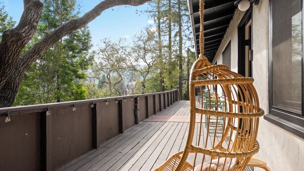 A wooden deck with a wicker chair and a hanging swing, overlooking a forested area. - Serene Mill Valley Retreat - King Bed, Walk to Downtown, Deck, Sleeps 4. (Mill Valley)
