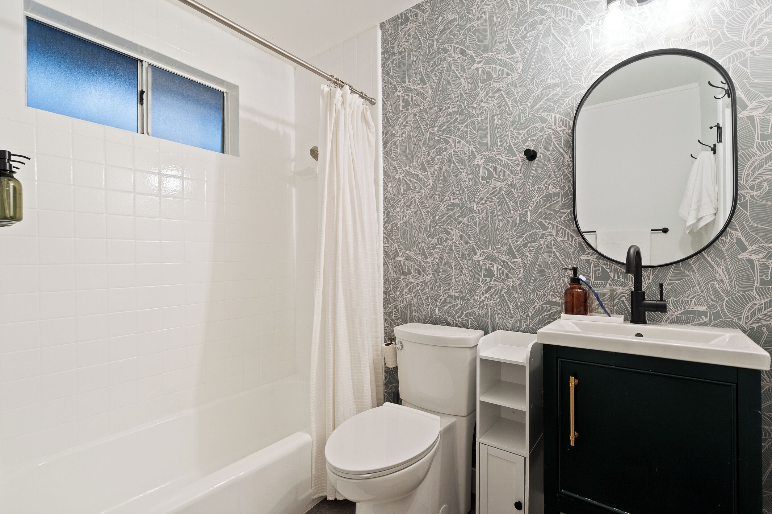 A bathroom with a white toilet, a bathtub, a shower curtain, a sink with a mirror, and a patterned wall.