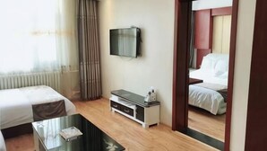 A hotel room with a bed, a TV, a coffee table, and a mirror. - Jinma Hotel (Qiqihar)