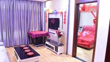 A room with a massage table, a TV, and a bed with red bedding.