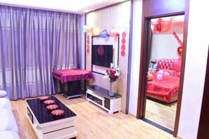 A room with a massage table, a TV, and a bed with red bedding.