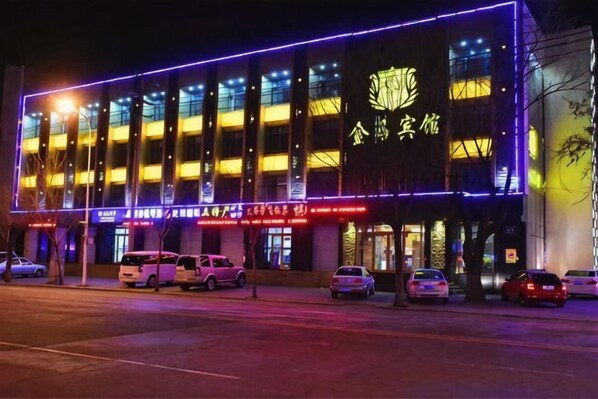Un edificio de varios pisos iluminado con luces de neón y varios automóviles estacionados al frente.