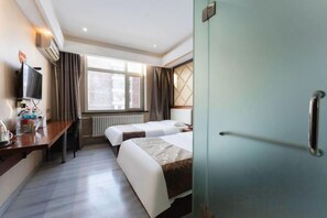 Habitación de hotel con dos camas, un escritorio, un televisor y una ventana con cortinas.