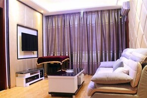 Een moderne woonkamer met een bank, een salontafel, een flatscreen-tv en een groot raam met gordijnen.