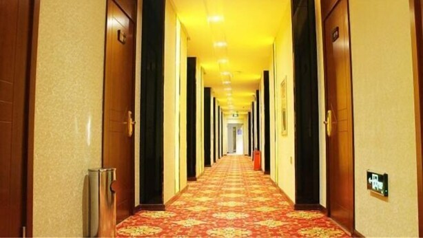 A hotel hallway with a carpeted floor, wooden doors, and a light fixture on the ceiling. - Jinma Hotel (Qiqihar)