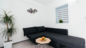 Ein modernes Wohnzimmer mit einem dunkelgrauen Sofa, einem runden Couchtisch mit Obst, einer Topfpflanze und einem Wandbild.