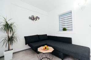 A modern living room with a dark grey sofa, a round wooden coffee table with fruit, a potted plant, and a wall-mounted decorative piece. - Excellent Central Apartment - Fira Towm (Fira)