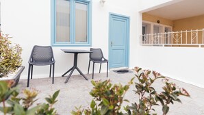 Eine kleine Außenveranda mit Tisch und zwei Stühlen, einer blauen Tür und einer weißen Wand.