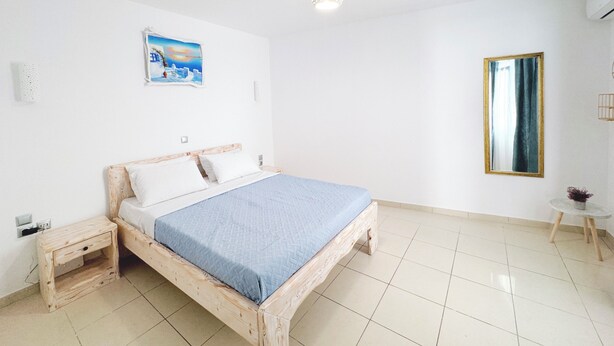 Ein Schlafzimmer mit einem hölzernen Bett, einem Nachttisch, einem kleinen Tisch, einem Spiegel und einem Gemälde an der Wand.