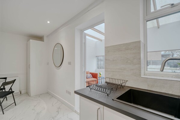 A modern kitchen with a black countertop, a sink, and a window above it. - Spacious 2-Bedroom Home in Edgware (HA8) (Edgware)