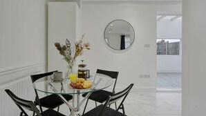 En matplats med ett glasbord, svarta stolar, en vas med blommor och en frukostuppsättning med bland annat croissanter och apelsinjuice.