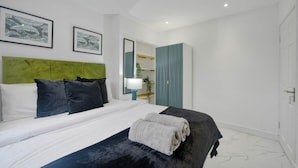 Ett modernt hotellrum med en säng, en grön sänggavel, två inramade tavlor, en spegel och en garderob.