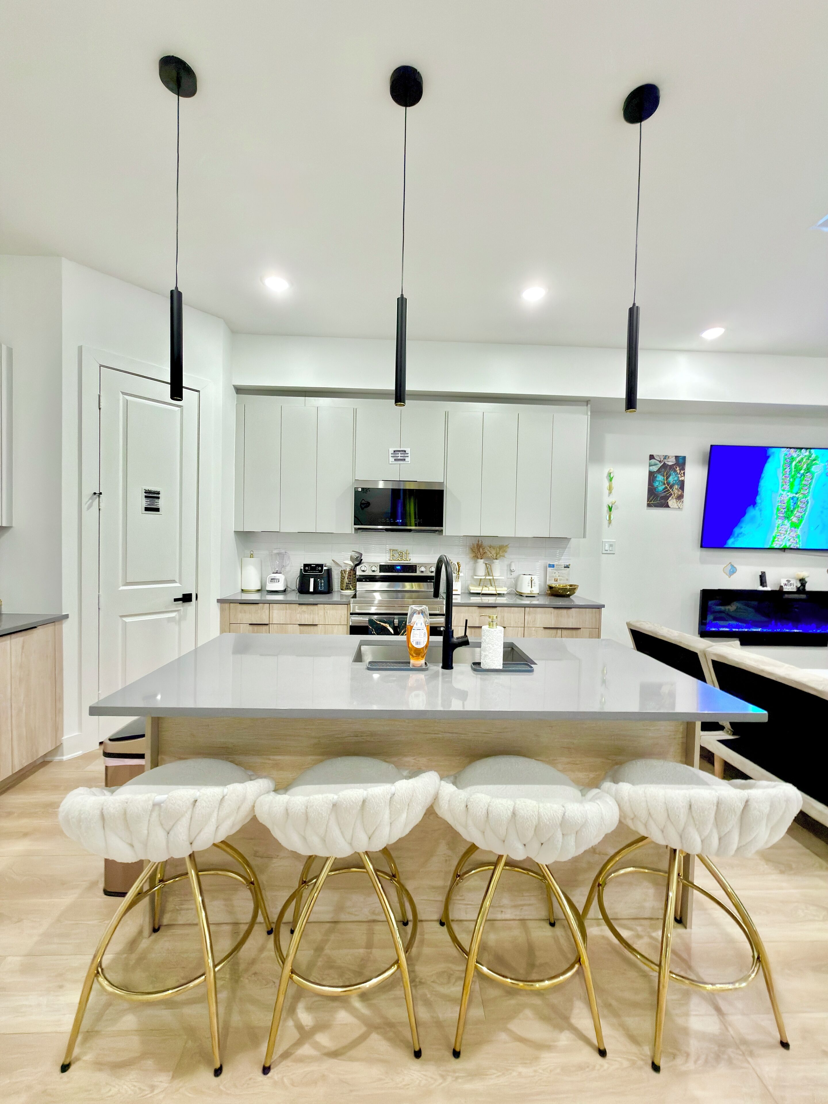 A modern kitchen with a central island, bar stools, and a flat-screen TV.