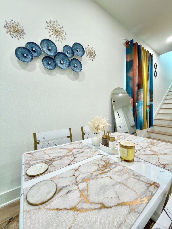 A dining area with a marble table, decorative wall art, and a staircase with colorful curtains.