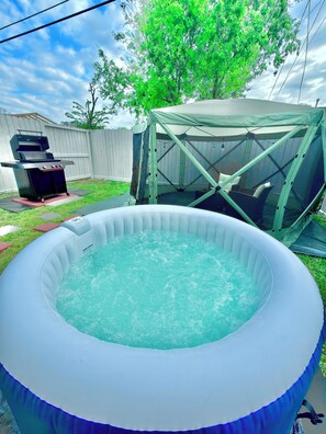 An inflatable pool with a hot tub, a barbecue grill, and a tent structure in a backyard.