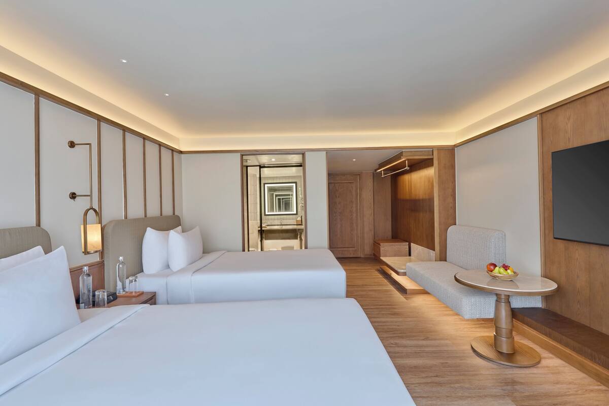A hotel room with two beds, a small table with fruit, a sofa, and a TV.
