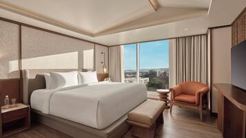 A modern hotel room with a large bed, a wooden bench, a television, and a view of the cityscape.