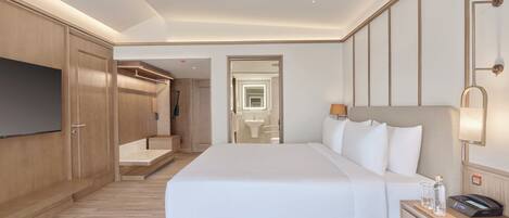 A hotel room with a large bed, a TV, a bedside table with a lamp, and a bathroom visible through an open door.