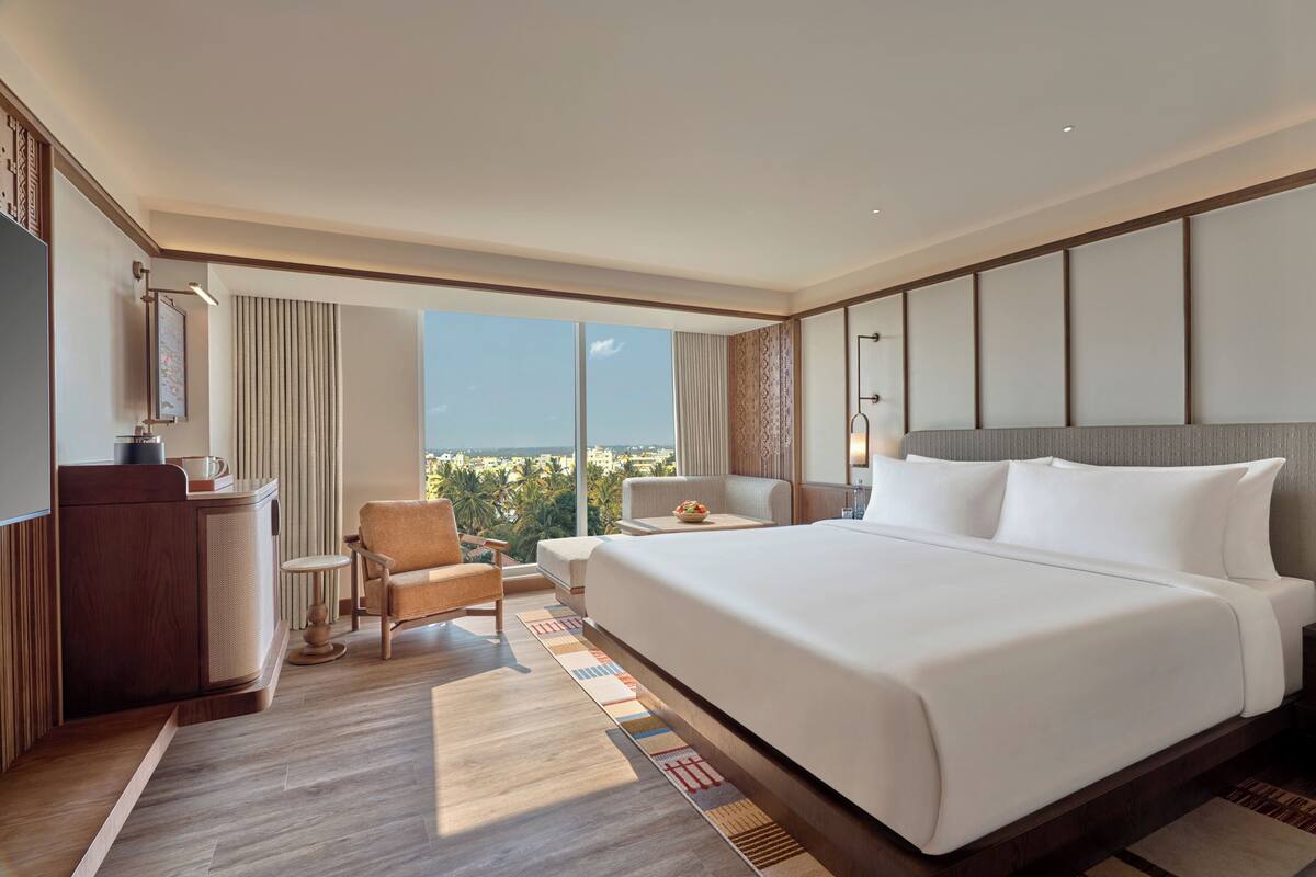 A hotel room with a large bed, a desk, a chair, and a view of the city.