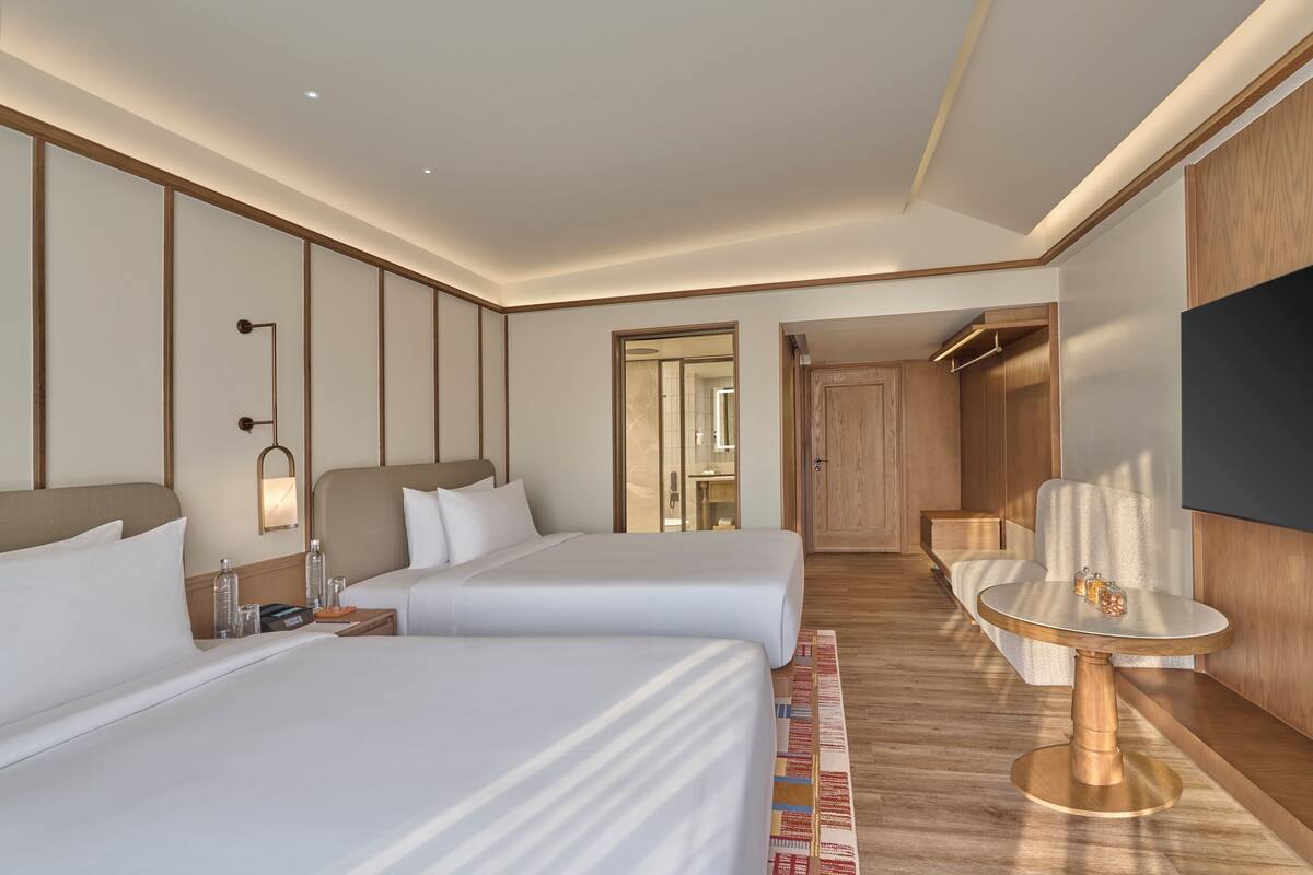 A hotel room with two beds, a small table, a TV, and a mirror.