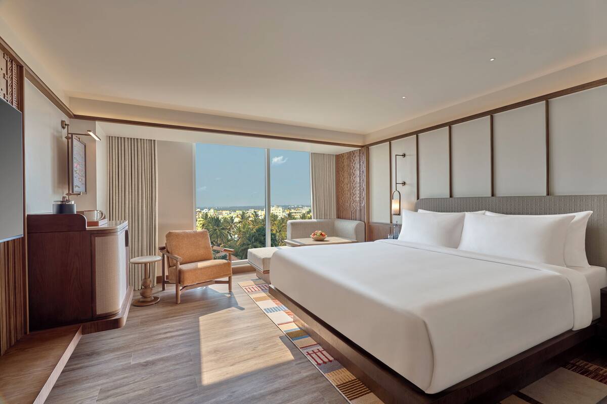 A hotel room with a large bed, a desk, a chair, and a view of the city.