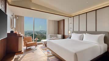 Habitación de hotel con una cama grande, un escritorio, una silla, un televisor y vistas a la ciudad.