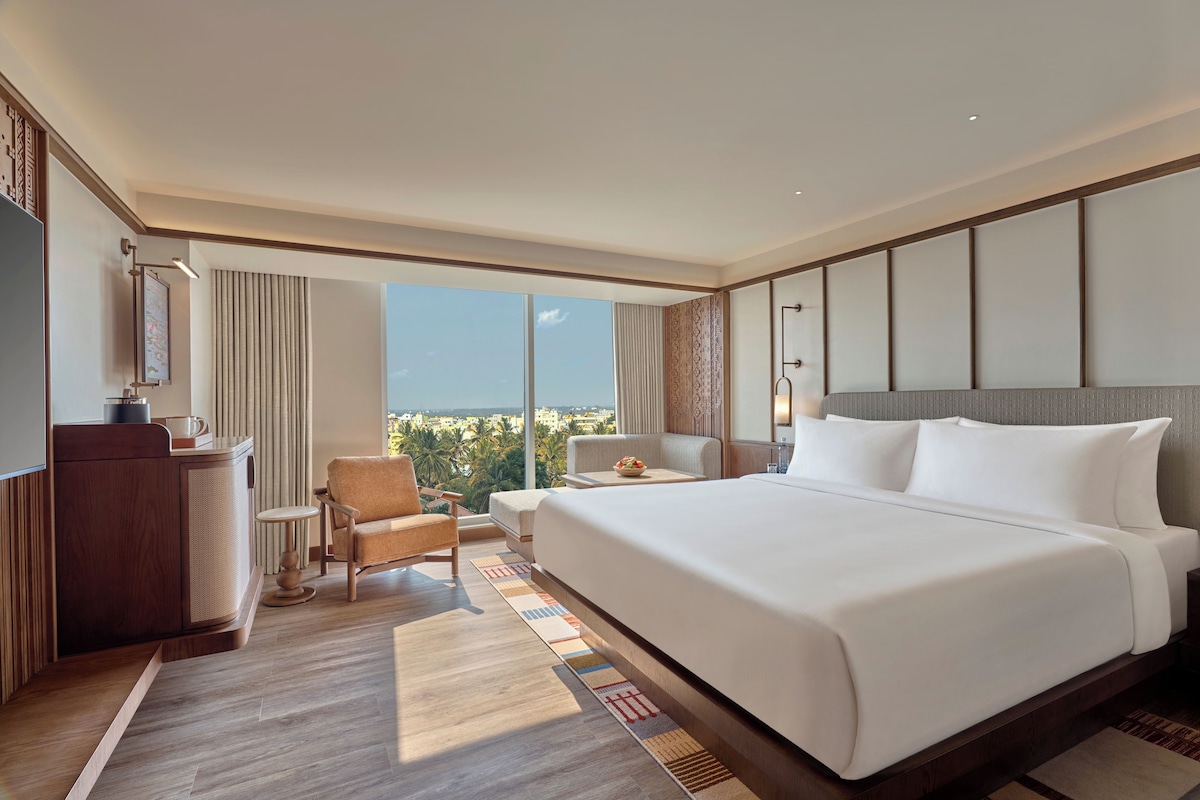 A hotel room with a large bed, a desk, a chair, and a view of the city.